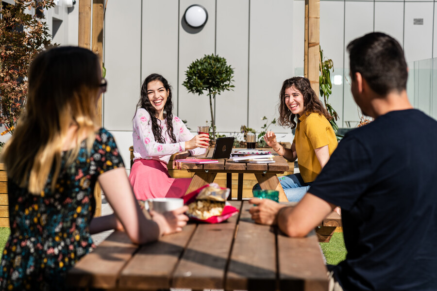 Four students sat at picnic benches laughing on a sunny day