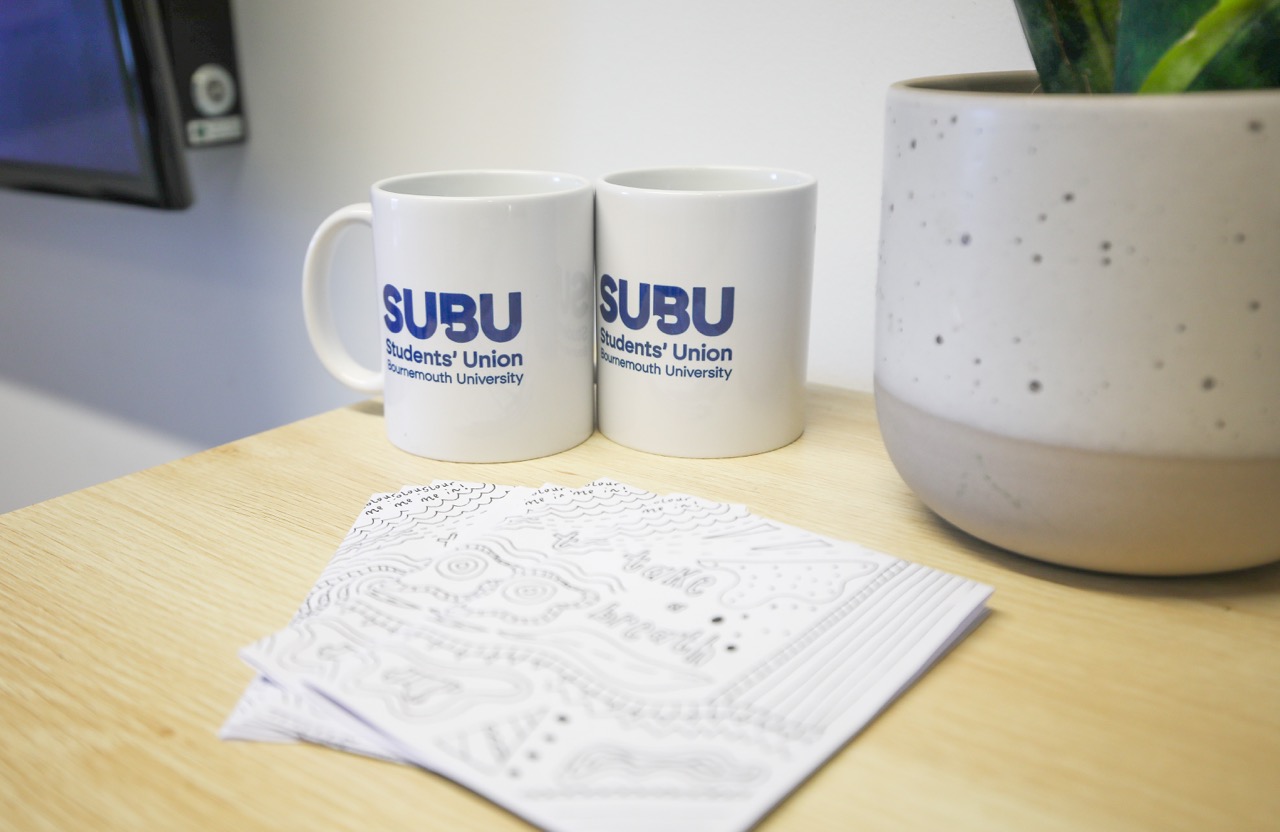 Two coffee mugs on a desk with paperwork