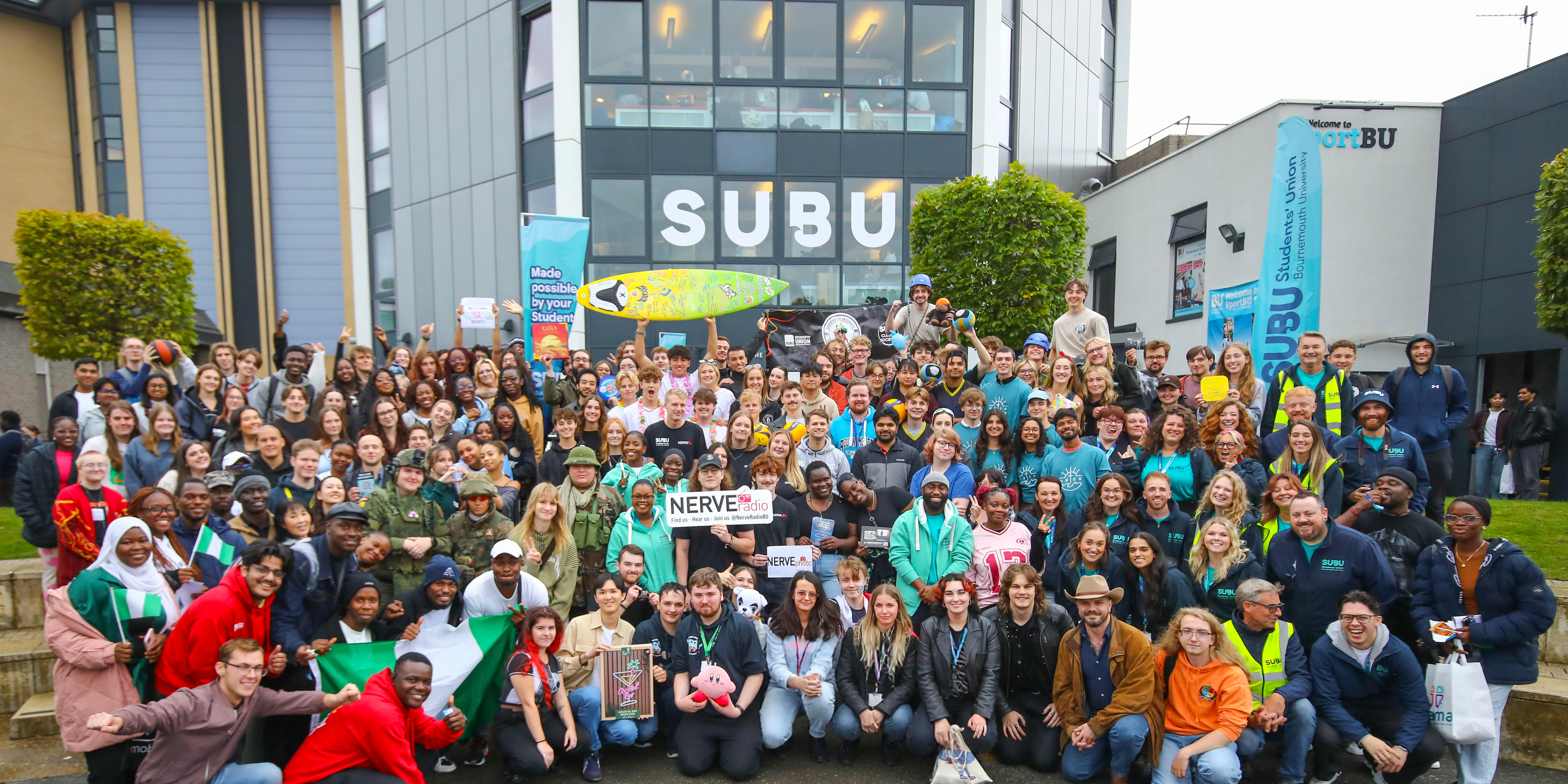 A crowd of SUBU Staff and Students after the Fresher Fair, including various branding and props from specific clubs and societies