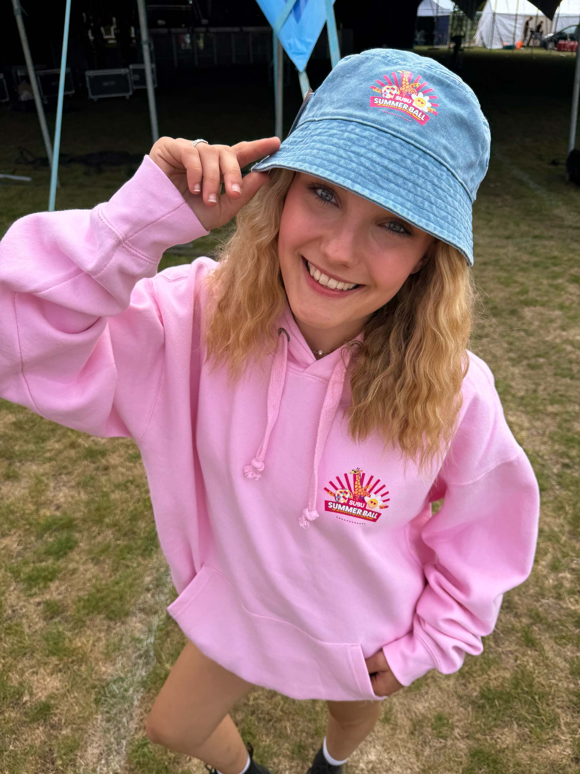 A student wearing a pale pink SUBU Summer Ball hoodie and a denim SUBU Summer Ball bucket hat